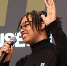 Me mid-talk, microphone in one hand, the other raised