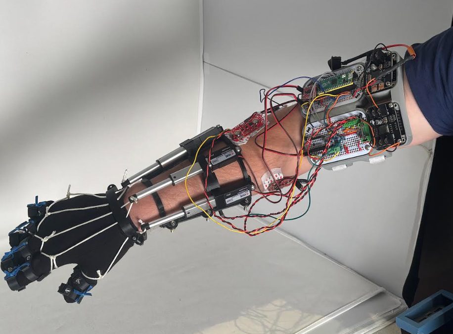 The whole device off the arm on a table: two breadboards, three sEMG pads, three actuators, a battery in a printed box