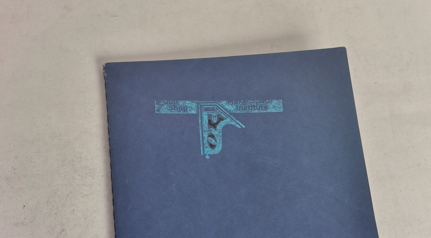 A blue notebook with the Makerspace Institute logo pressed into the cover in teal foil