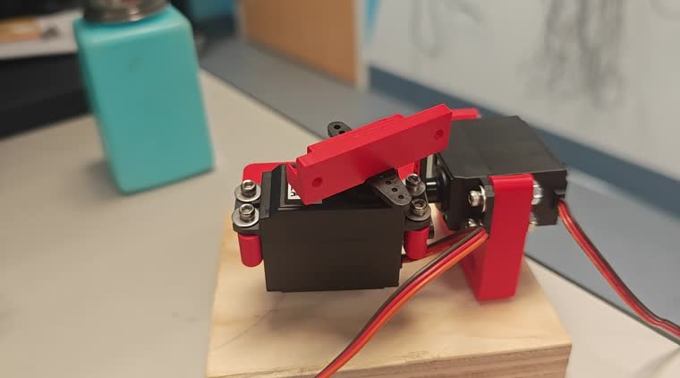 The pan-tilt spotlight built during the workshop, a red and black 3D printed servo linkage moving on a wooden block